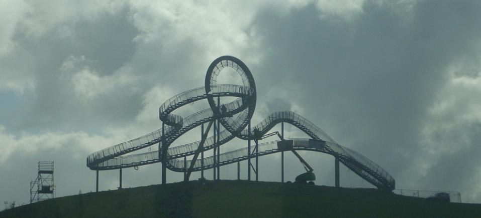 Eine Achterbahn auf dem Gipfel eines Hügels mit einer bewölkten Himmel, umgeben von Stützpfählen und -strukturen.