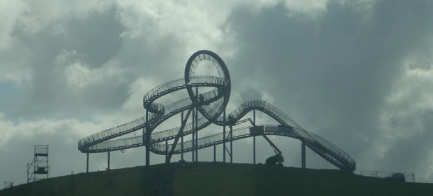 Eine Achterbahn auf dem Gipfel eines Hügels mit einer bewölkten Himmel, umgeben von Stützpfählen und -strukturen.