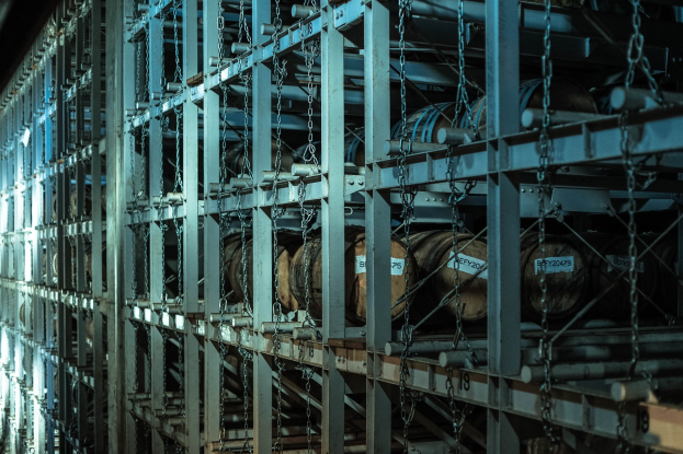 Großes Lager mit zahlreichen Fässern, die in Metallregalen gestapelt und mit Stangen und Ketten gesichert sind, organisiert für eine effiziente Lagerung.