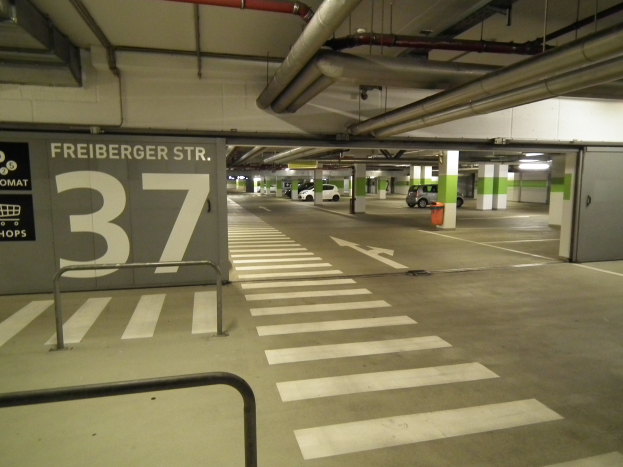 Eine Tiefgarage mit einem "Freiburger St." Schild, mehrere geparkte Fahrzeuge, Säulen, ein Feuerhydrant und eine Decke mit sichtbaren Rohren.